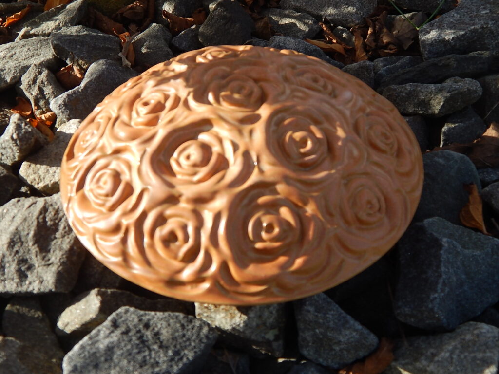 Tierurne in Diskusform, Sand mit Rosenblüten